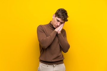 Handsome young man over isolated yellow background making sleep gesture in dorable expression