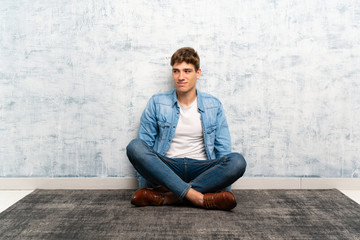 Handsome young man sitting on the floor standing and looking to the side