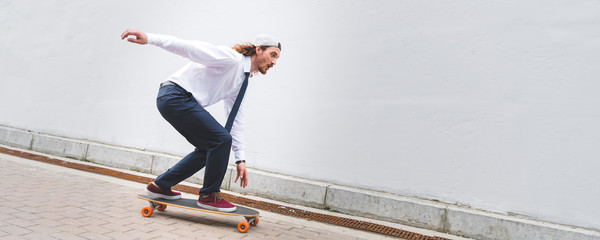 Panoramic view of handsome businessman riding on skateboard at street