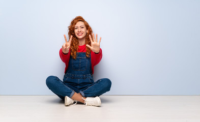 Redhead woman with overalls sitting on the floor counting seven with fingers