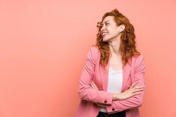 Redhead woman in suit over isolated pink wall standing and looking to the side