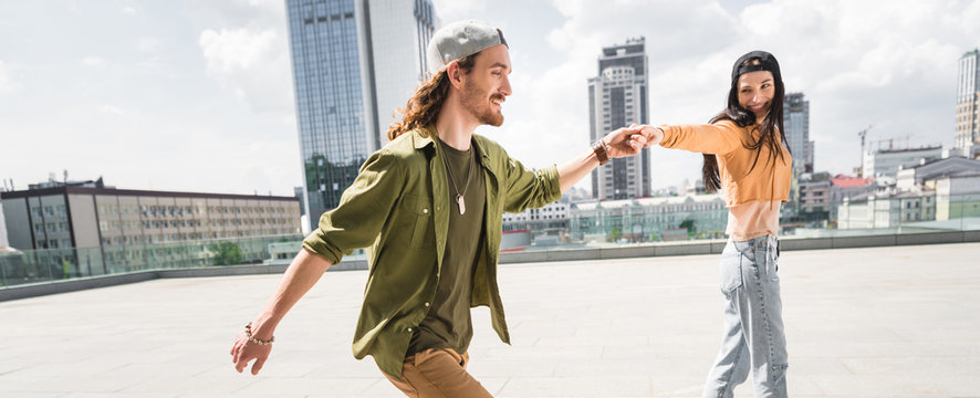 panoramic view of happy couple in casual wear holding hands, walking on city - Powered by Adobe