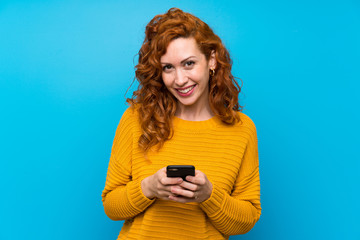 Redhead woman with yellow sweater sending a message with the mobile