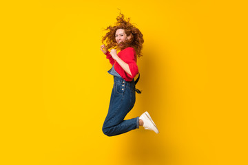 Fototapeta na wymiar Redhead woman with overalls jumping over isolated yellow wall