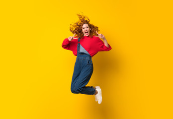 Fototapeta na wymiar Redhead woman with overalls jumping over isolated yellow wall