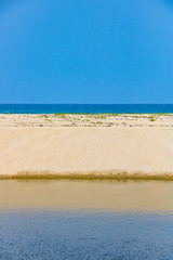 dead straight sand beach at the ocean with blue sky as an absolutely straight abstract line formation