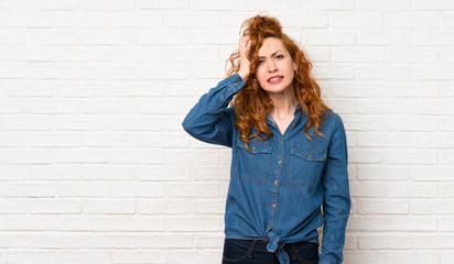 Redhead woman over white brick wall with an expression of frustration and not understanding