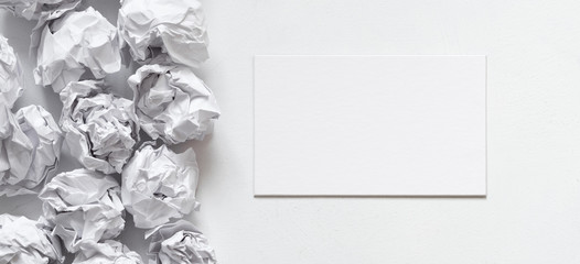 Business idea. Flat lay of blank card and crumpled paper ball pile on white background. Copy space.