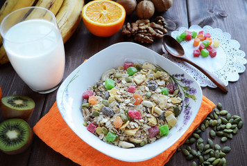Muesli with candied fruits and nuts with a glass of milk on a dark wooden table.
