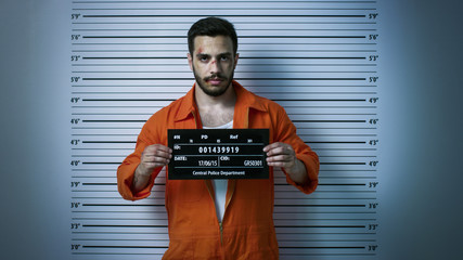 In a Police Station Arrested Man Getting Front-View Mug Shot. He's Wearing Prisoner Orange Jumpsuit...