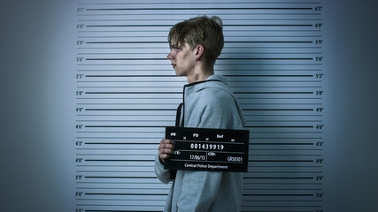 In a Police Station Arrested Drug Addict Teenage Posing for a Side View Mugshot. He is Heavily...
