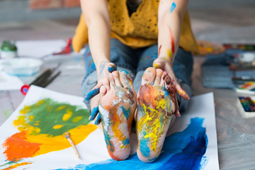 Art therapy. Cropped shot of artist sitting on floor, showing feet and hands dirty with multicolor...