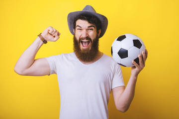 Goal! Exciter winner bearded man holds a football ball smiling on yellow background.