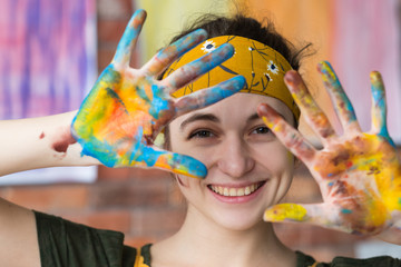 Art therapy. Closeup portrait of young female artist having fun in studio, smiling, showing hands dirty with paint. - obrazy, fototapety, plakaty