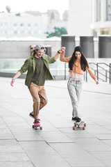 happy man holding hands with beautiful woman, riding on skateboard in city © LIGHTFIELD STUDIOS