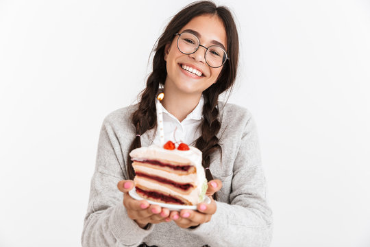 Photo closeup of joyful teenage girl wearing eyeglasses smiling while holding big slice of birthday cake