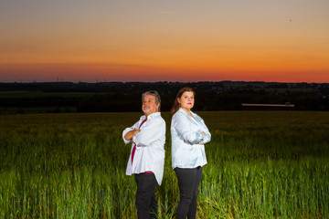 Man and woman stand putting their backs at each other as disagreement, at end of the day out in the field with the beautiful landscape that nature presents with the sunset.