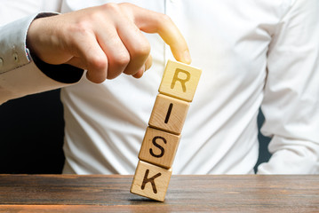 Businessman rescues with his finger a tower of cubes with the word Risk from falling Risk management, cost assessment, business and investment safety. Strengthen business resilience and flexibility.