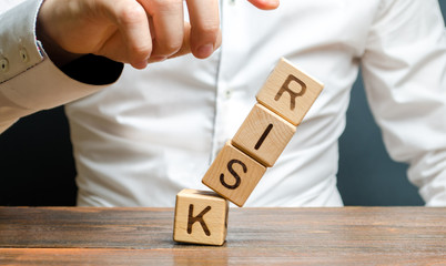A businessman knocks down a tower of cubes with the word Risk. Risk management, cost assessment, business and investment safety. Strengthen business resilience and flexibility. Could not avoid failure