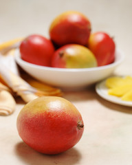 Delicious and healthy,  ripe mangos in a bowl with plate of cut fruit on a softly colored table cloth