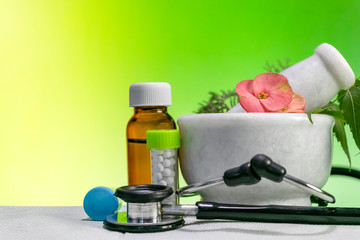 Alternative medicine concept – Homeopathic Healing herbs with a mortar and pestle with Stethoscope along with bottle of pills and liquid homeopathic substance.