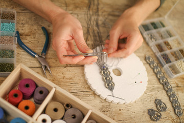 Close up of female hands making a macramé bracelet with kumihimo on a wooden table with tools,...