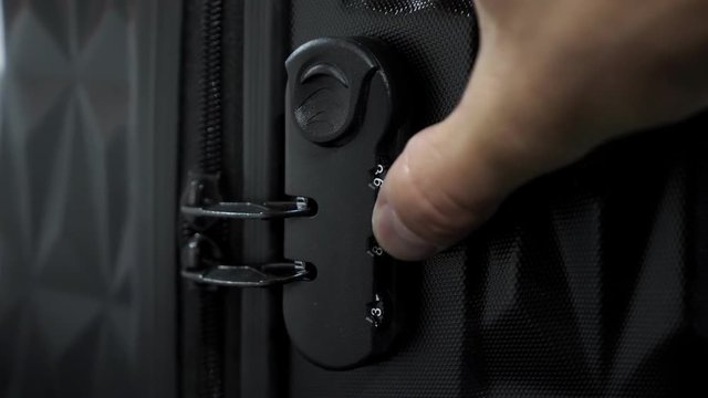 Man is testing lock. He enters the code to open suitcase combination lock on the suitcase and presses the button, hands closeup.
