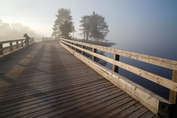 Morning misty landscape with old wooden bridge and trees suluets, Valaam Island, Karelia, Russia.