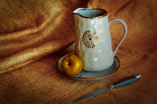 Kitchenware for villagers. Nutrmort with jugs, an apple and a knife. Warm fabric background. Autumn tones. Rustic style