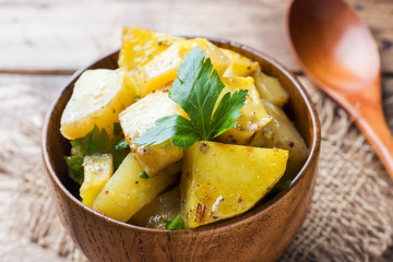 Baked potatoes with spices and herbs in wooden plate.
