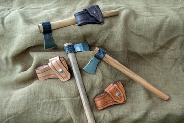 Three hand forged tomahawks and leather sheaths displayed on burlap with bokeh effect. The hawks...