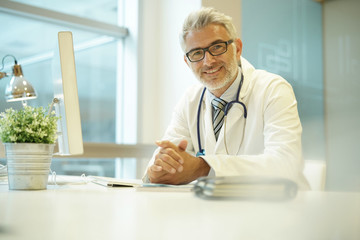 Portrait of handsome mature doctor sitting at desk in modern office