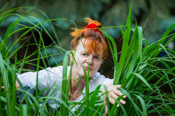 A curious woman is standing in a garden between plants and secretly observes. Concept curious...