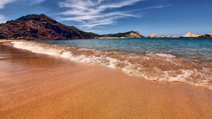 view from the sand of a menorca cove of crystal clear turquoise water.