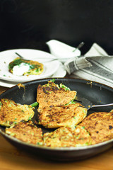 Proper nutrition, vegetarian breakfast gluten free,zucchini courgette pancakes with beans, mint on frying pan with sour greek yogurt, black background, towel, fork, knife on wooden surface