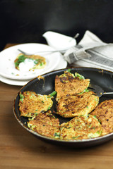 Proper nutrition, vegetarian breakfast gluten free,zucchini courgette pancakes with beans, mint on frying pan with sour greek yogurt, black background, towel, fork, knife on wooden surface