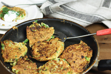 Proper nutrition, vegetarian breakfast gluten free,zucchini courgette pancakes with beans, mint on frying pan with sour greek yogurt, black background, towel, fork, knife on wooden surface