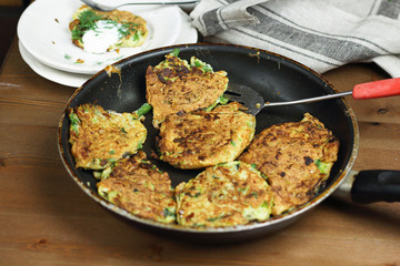 Proper nutrition, vegetarian breakfast gluten free,zucchini courgette pancakes with beans, mint on frying pan with sour greek yogurt, black background, towel, fork, knife on wooden surface