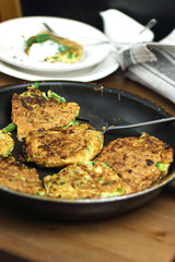 Proper nutrition, vegetarian breakfast gluten free,zucchini courgette pancakes with beans, mint on frying pan with sour greek yogurt, black background, towel, fork, knife on wooden surface
