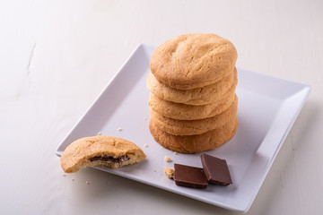 Homemade stack of shortbread chocolate cookies with one bitten cookie and two pieces of chocolate on white plate wooden table
