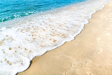 Ocean wave on tropical beach with golden sand and ripple of water splash from emerald blue-green sea water during summer vacation. 