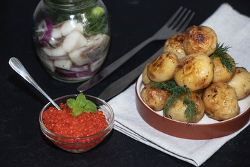 Boiled and roasted young potatoes, red caviar in a transparent scallop, herring sliced.