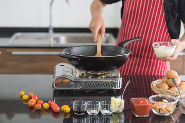 Cropped view of man prepare cooking food in black pan, holding bowl of slice onion