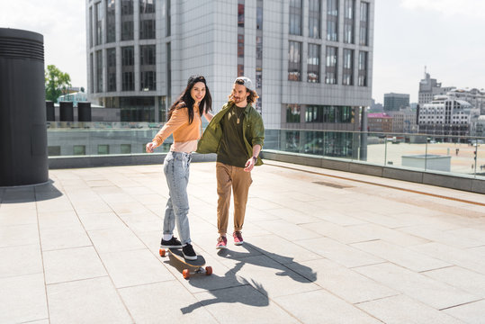 happy woman holding hands with man, riding on skateboard on roof