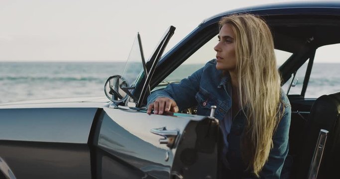Portrait of soulful attractive woman looking out of a classic vintage sports car by the ocean with the wind blowing in her hair, woman going on a road trip