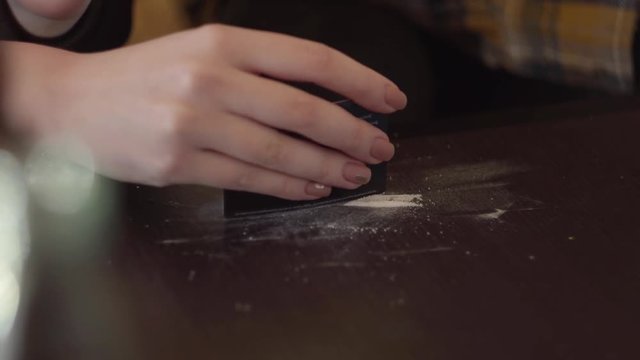 Hand of young drug addict woman making cocaine line with black credit card on wooden surface at home close-up. Drug addicted woman. Troubled teens