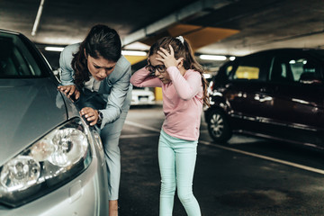Frustrated and terrified mother and daughter looking at their scratched car.