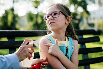 Mother spraying insect repellents on her daughter's skin.