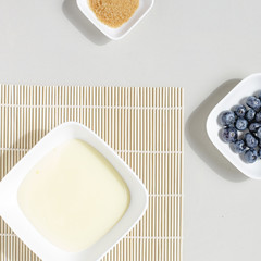 Vanillepudding, Blaubeeren, brauner Zucker in weißen Servierschalen auf weißem Holztisch,...