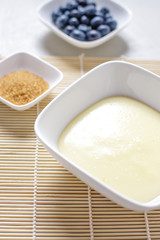 Vanillepudding, Blaubeeren, brauner Zucker in weißen Servierschalen auf weißem Holztisch, Ansicht...